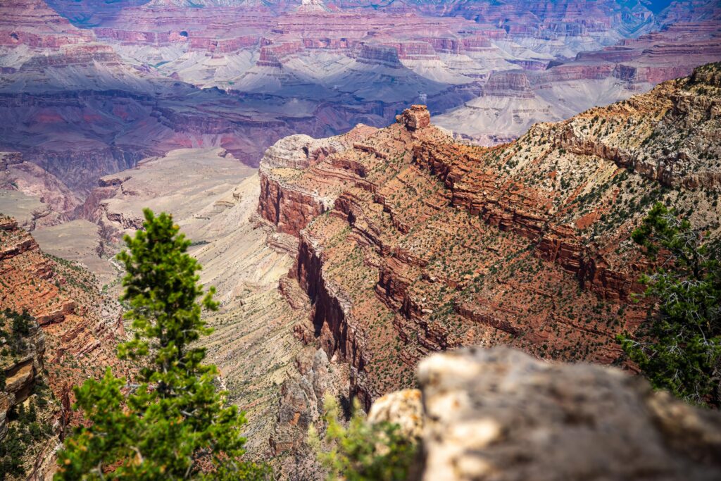 Vast canyon with red rock cliffs layered mountains and green foliage under natural sunlight wallpaper