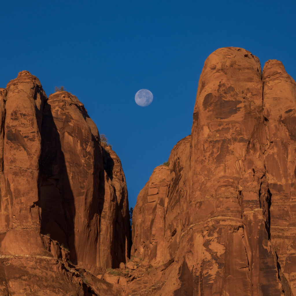 Towering canyon rocks bathed in warm light under full moon and clear blue sky wallpaper background