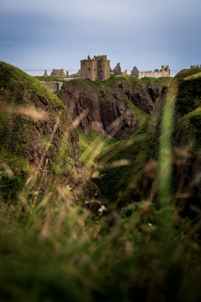 Majestic ancient castle on rugged cliff with lush green slopes under clear blue sky landscape wallpaper
