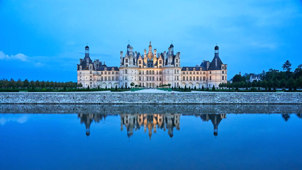 Château de Chambord at night illuminated reflecting on calm water under twilight sky wallpaper