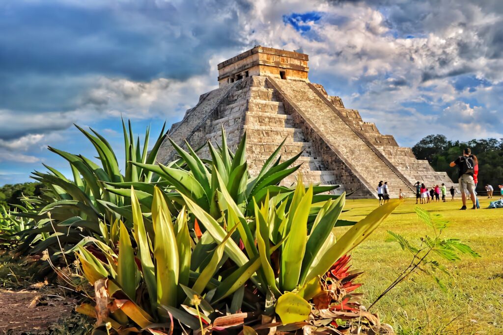 Chichén Itzá pyramid surrounded by lush greenery and dramatic clouds in vibrant wallpaper background