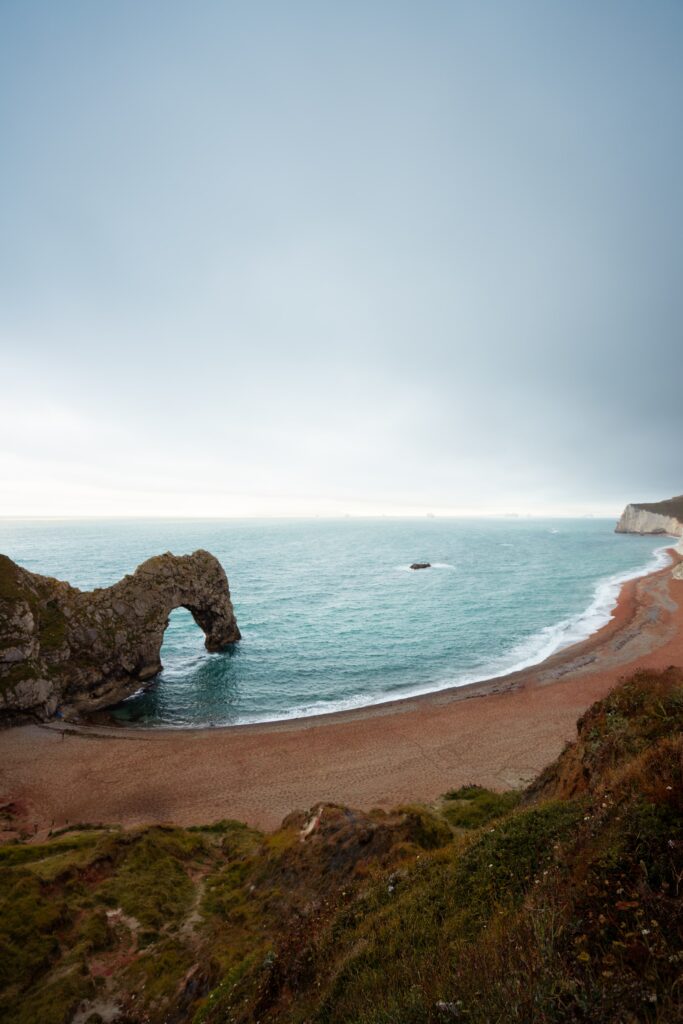 Dramatic coastal scene with rugged rocks natural stone arch gentle waves sandy shore wallpaper