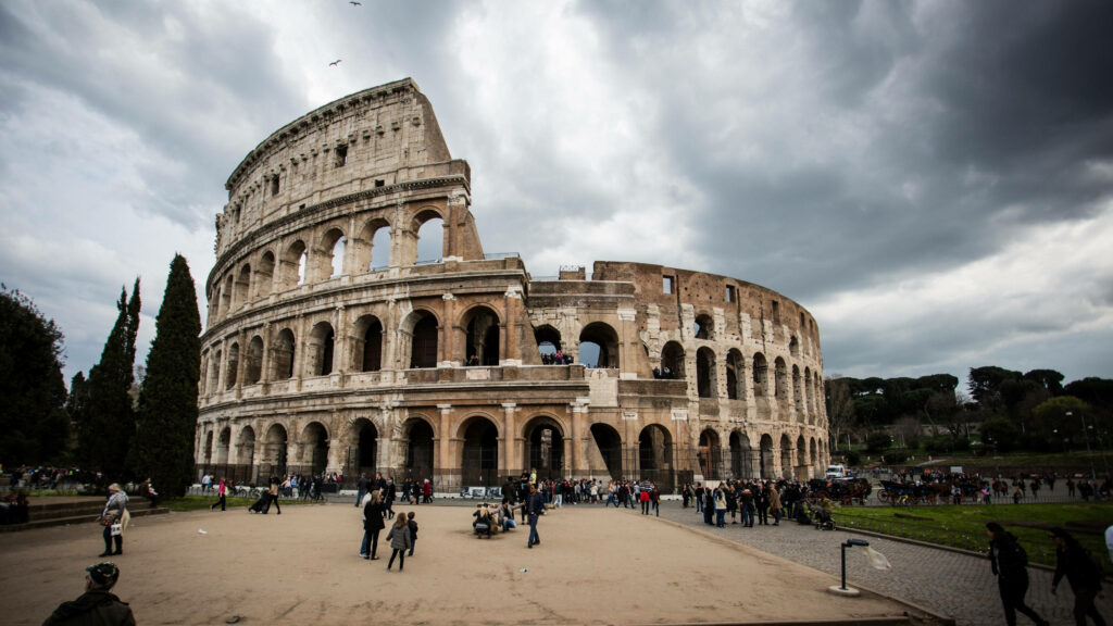 Colosseum in Rome under dramatic cloudy sky with lush greenery and visitors wallpaper background