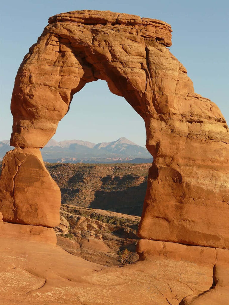 Close-up majestic Delicate Arch with reddish sandstone and rugged mountains under blue sky Wallpaper
