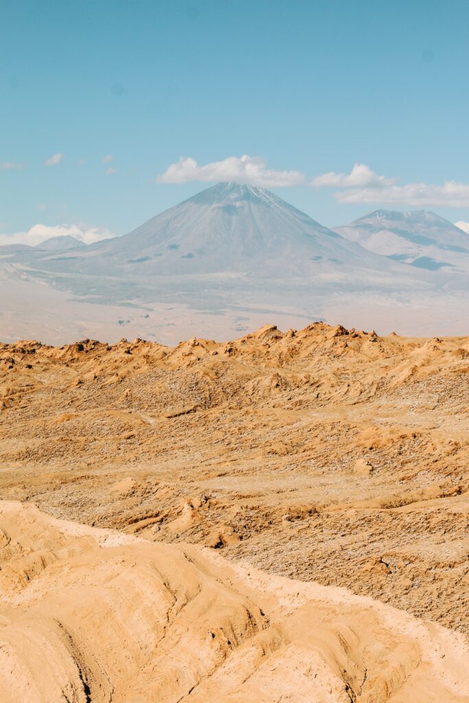 Breathtaking desert landscape with sandy foreground majestic volcano and rugged mountains under blue sky Wallpaper