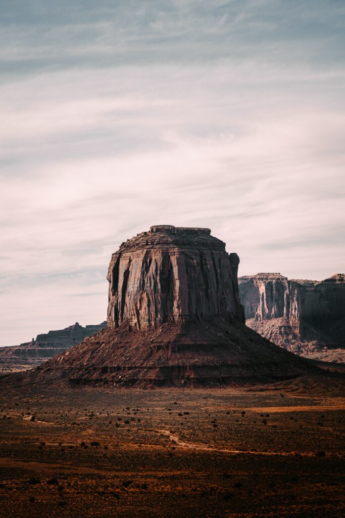 Majestic desert rock formation with rugged cliffs under soft light and blue sky background Wallpaper