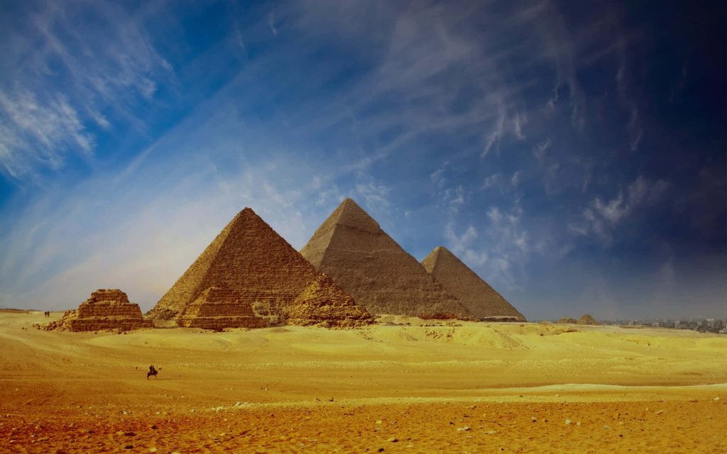 Giza Pyramids in golden Egyptian desert with camel rider under deep blue sky wallpaper background