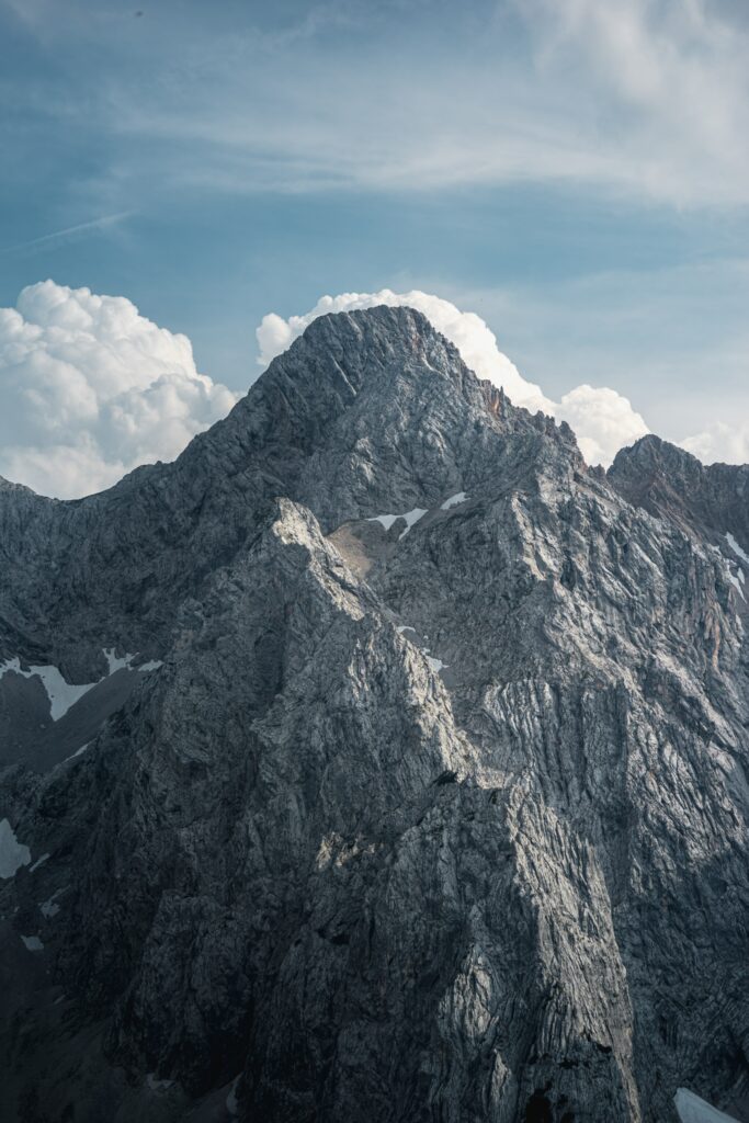 Majestic gray mountain peak with rugged rocks under swirling clouds and soft blue sky wallpaper