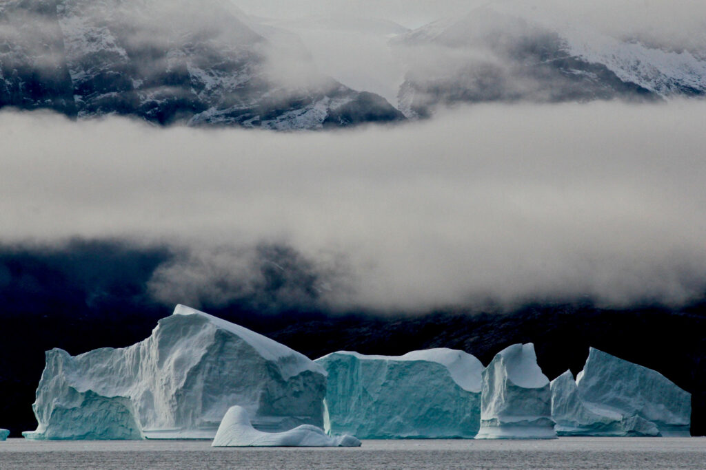 Majestic icebergs floating in chilly waters under misty mountains capturing Greenland ice cap beauty Wallpaper