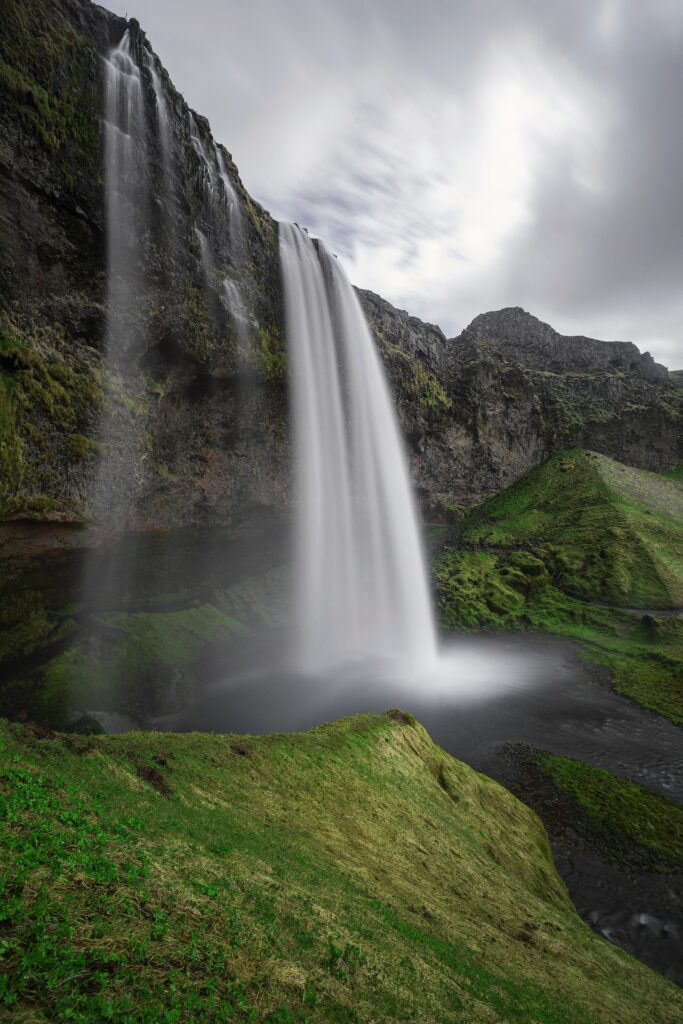 Majestic Icelandic waterfall over rugged rocks with green moss and cliffs under cloudy sky wallpaper