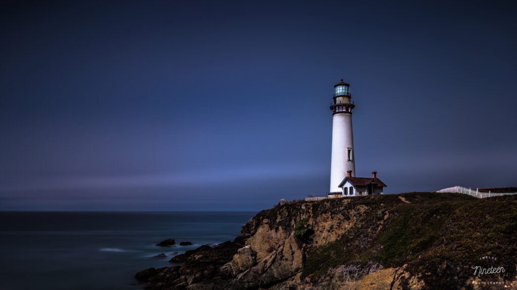 Majestic lighthouse on rugged cliff overlooking serene blue seascape peaceful coastal wallpaper