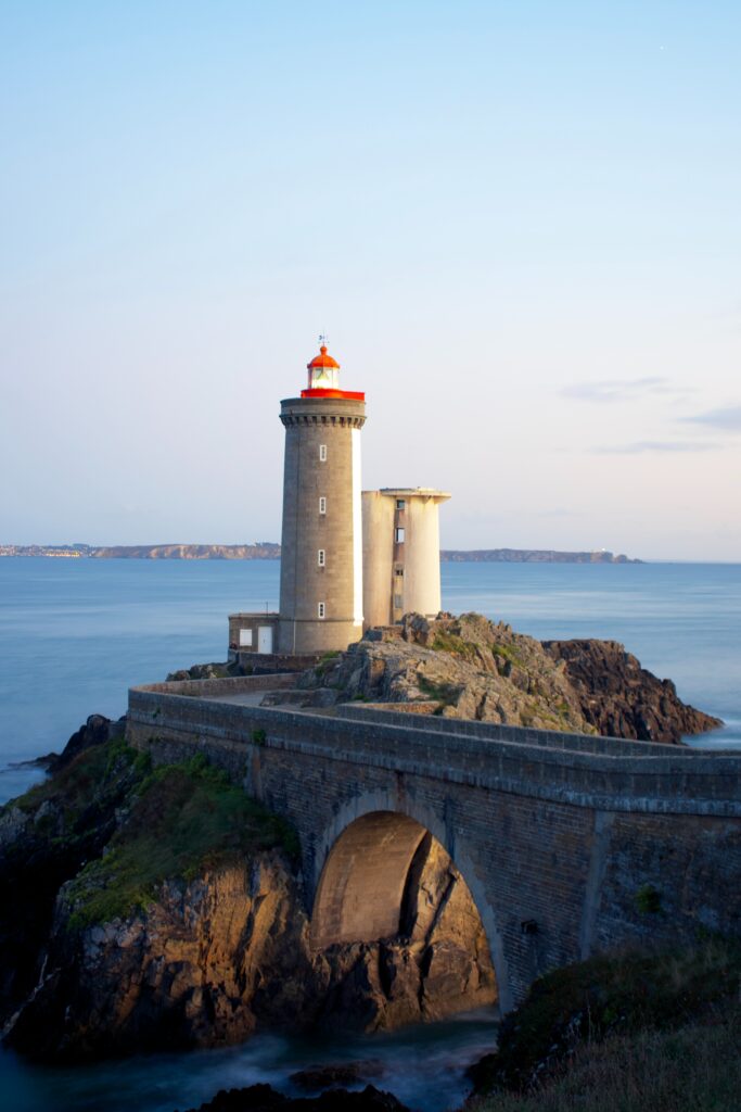 Majestic lighthouse on rocky coast glowing at dawn over tranquil sea with serene horizon background Wallpaper