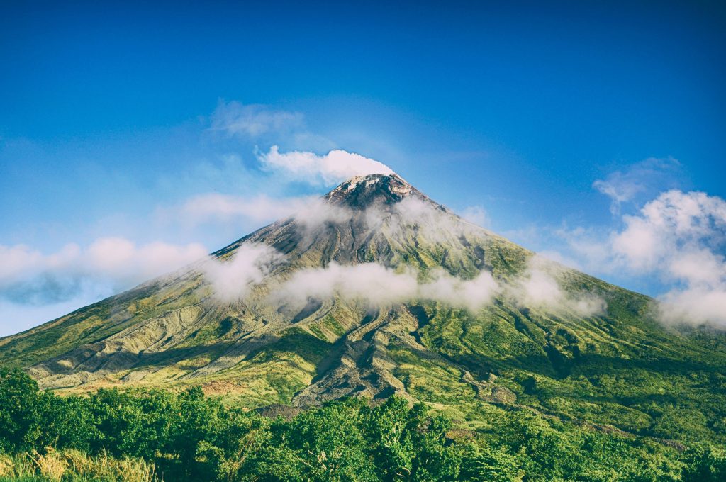 Mount Mayon volcano with perfect cone shape lush green slopes and wispy clouds under blue sky Wallpaper