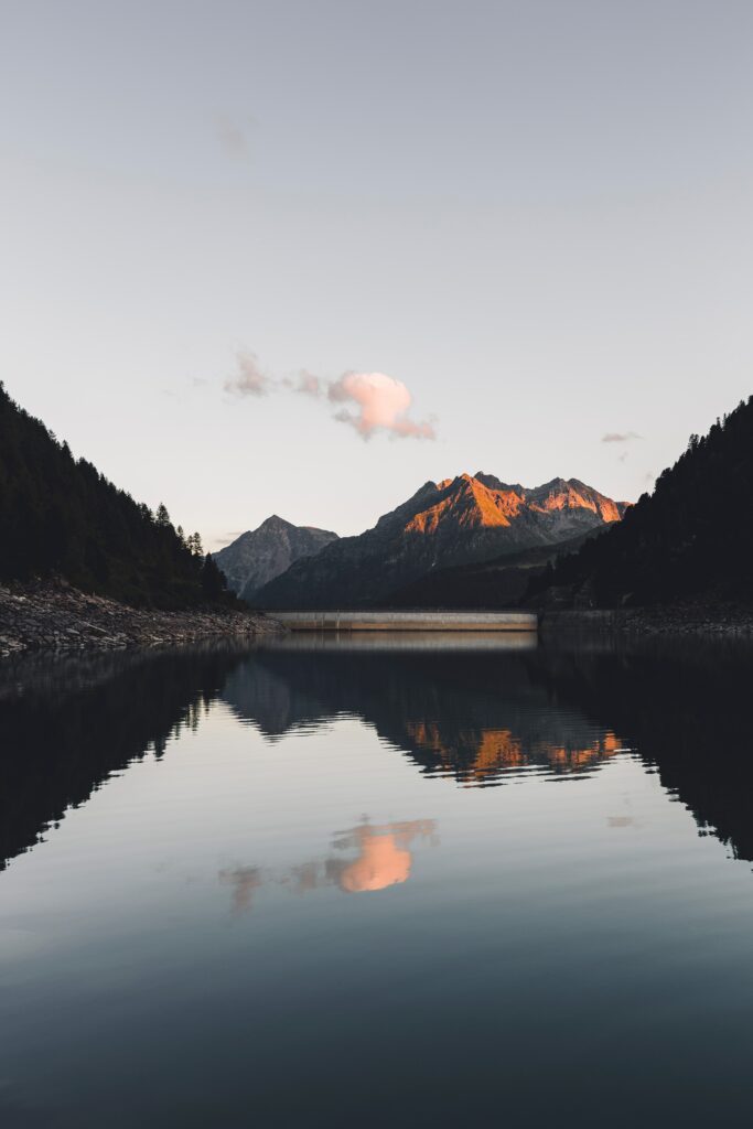Tranquil mountain landscape at sunset with calm lake reflections and dense surrounding forest Wallpaper
