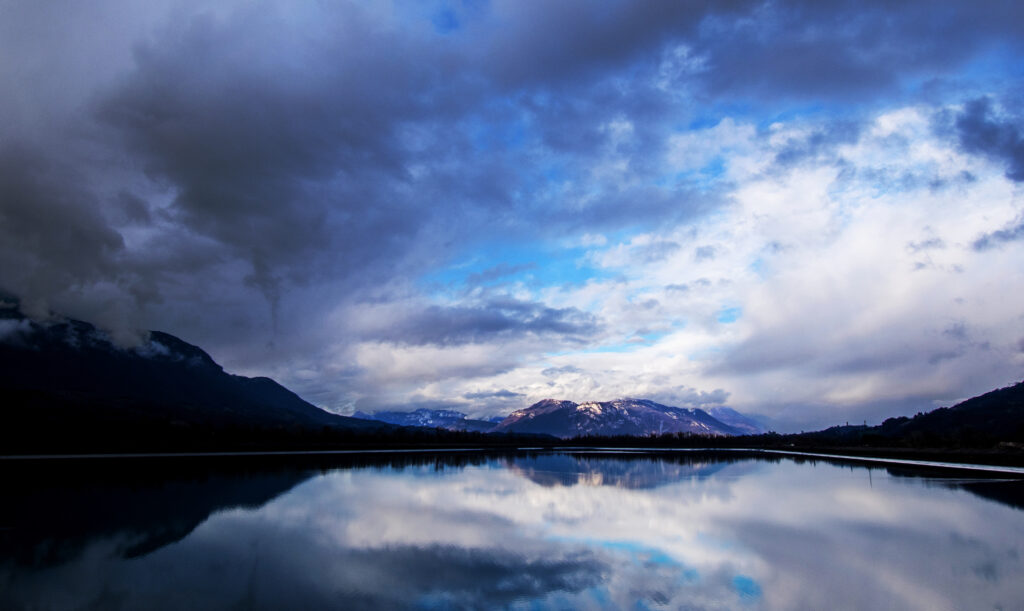 Majestic mountains reflected in a tranquil lake under dramatic swirling clouds and blue sky wallpaper