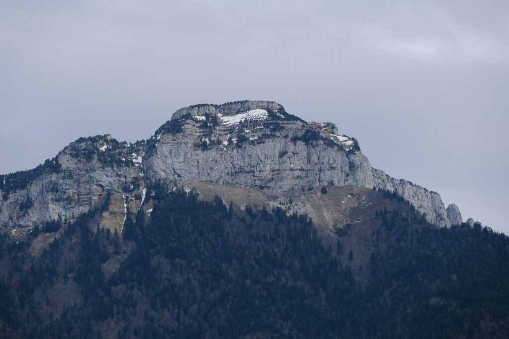 Majestic mountain with rugged cliffs and dense dark green forest under cloudy sky wallpaper