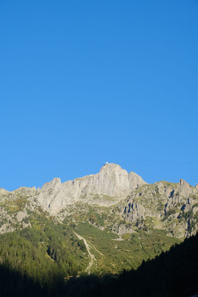 Dramatic mountain landscape with rugged rocks and dense green trees under vivid blue sky wallpaper