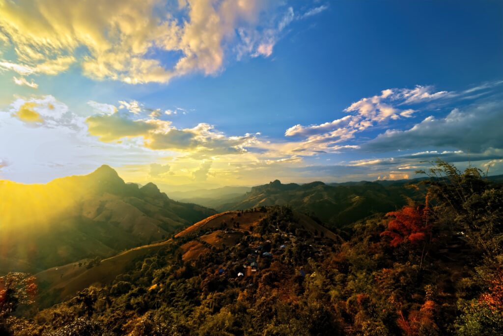 Breathtaking mountain landscape with sun rays through golden clouds and vibrant foliage below Wallpaper