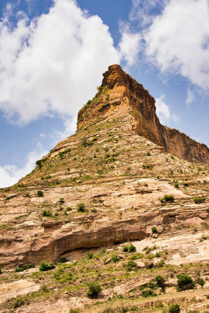 Majestic mountain peak with rugged rocks and green patches under blue sky and clouds wallpaper
