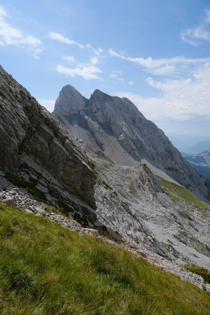 Majestic mountain peak with rugged rocks green grass and bright blue sky nature wallpaper background