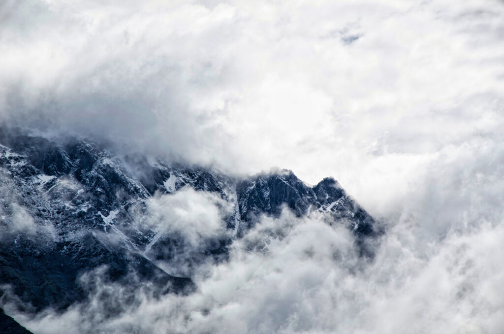 Majestic mountain peaks emerge through dense fog and clouds in a serene gray and white landscape Wallpaper