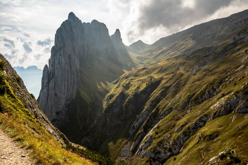 Majestic mountain peaks over rugged slope and deep gorge with sunlight and lush greenery Wallpaper
