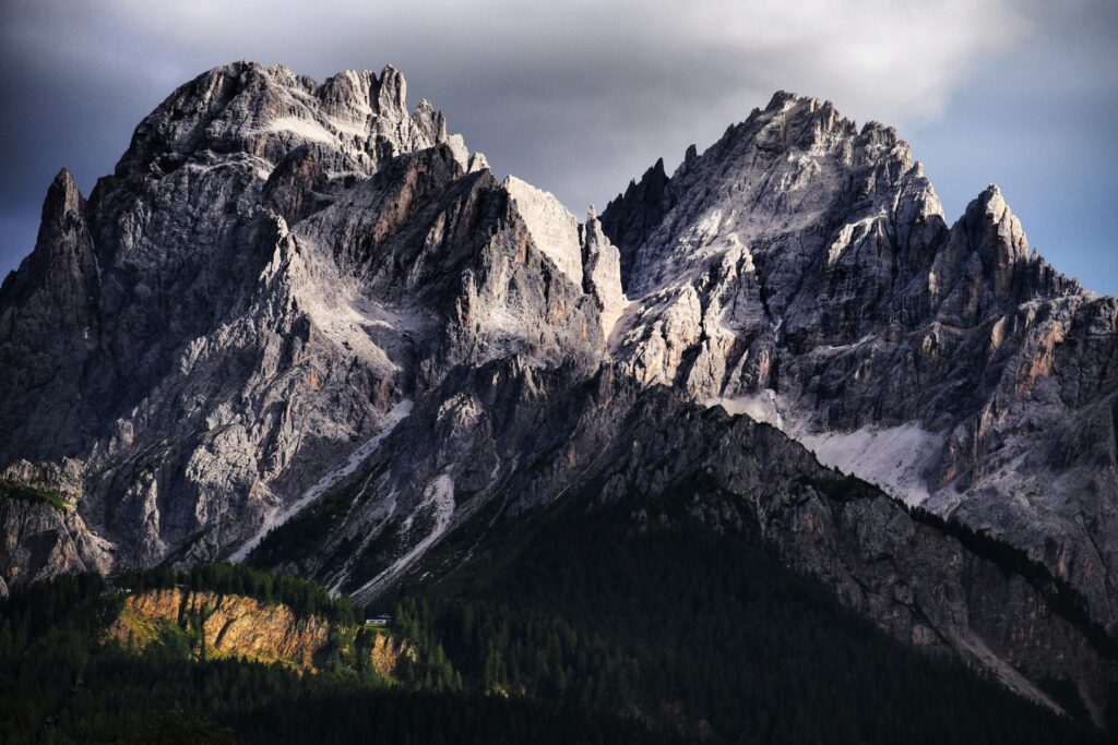 Towering mountain peaks with rugged rocks and dense forest in dramatic light and shadow wallpaper