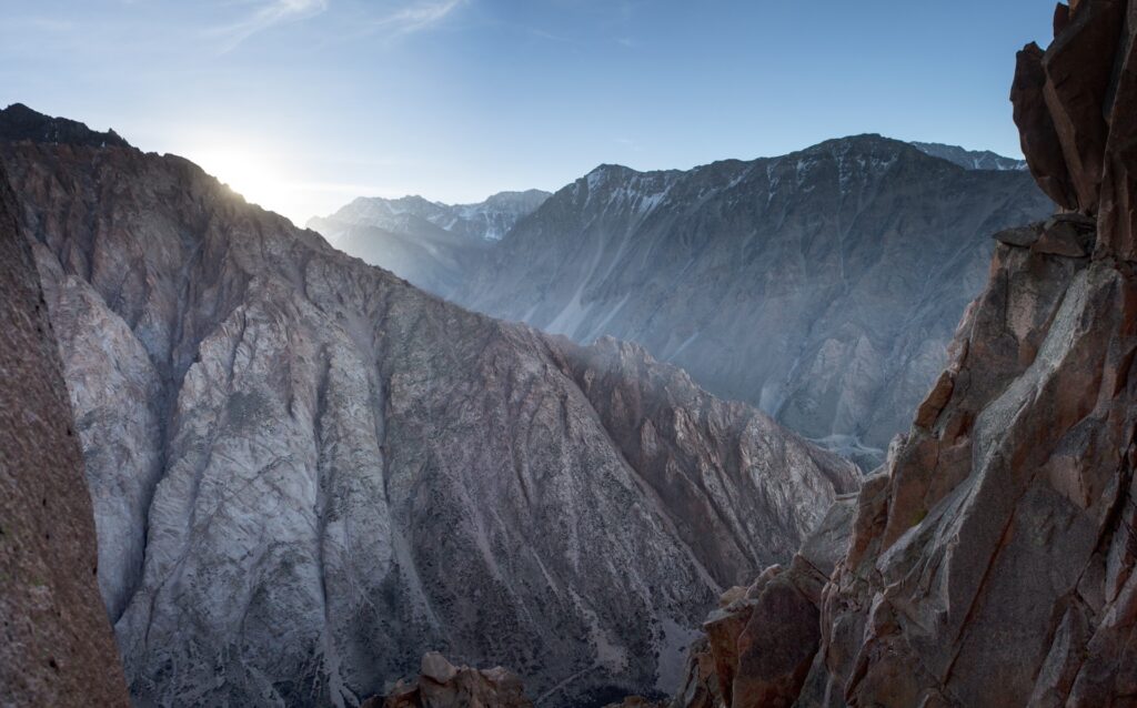 Towering mountain peaks and rugged rocks under clear blue sky with sunlight and shadows Wallpaper