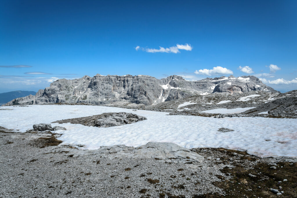 High-altitude landscape with rugged rocks melting snow vivid blue sky and distant mountain peaks Wallpaper