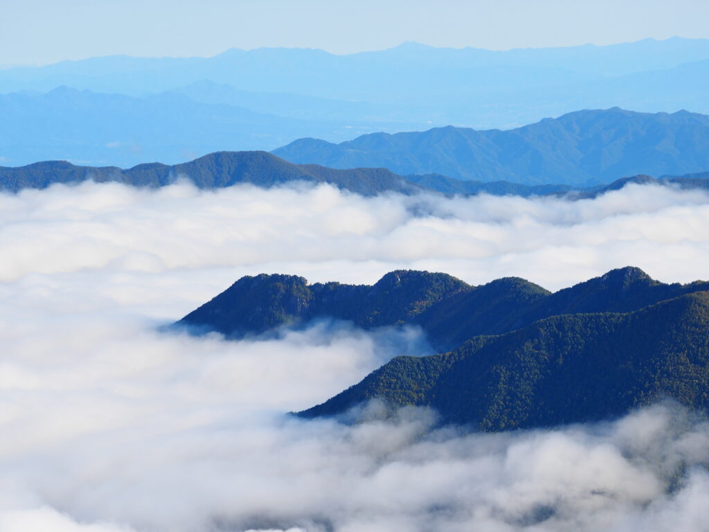 Aerial view of dark green mountain peaks above white clouds bathed in cool blue light wallpaper