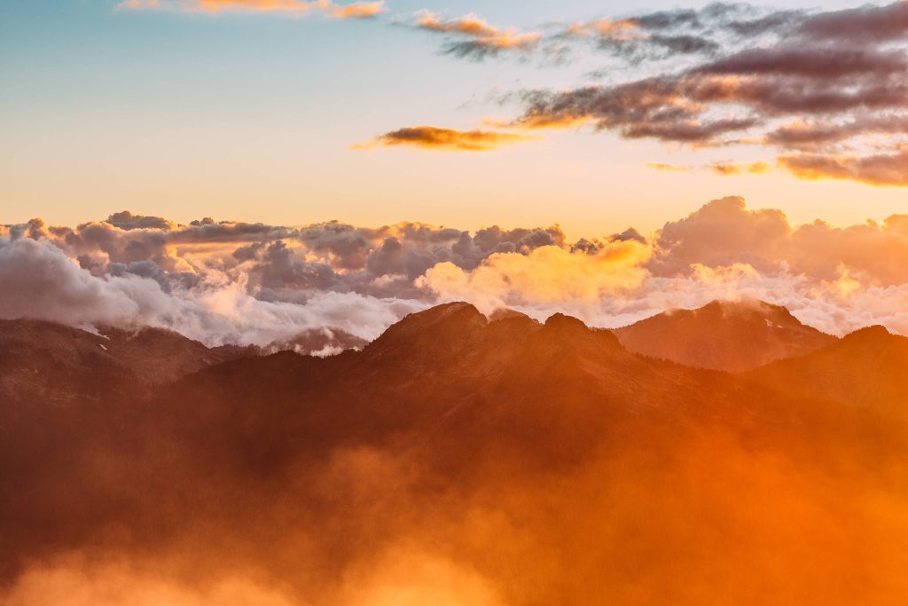 Majestic mountain range at golden hour sunset above clouds with warm light and shadows wallpaper