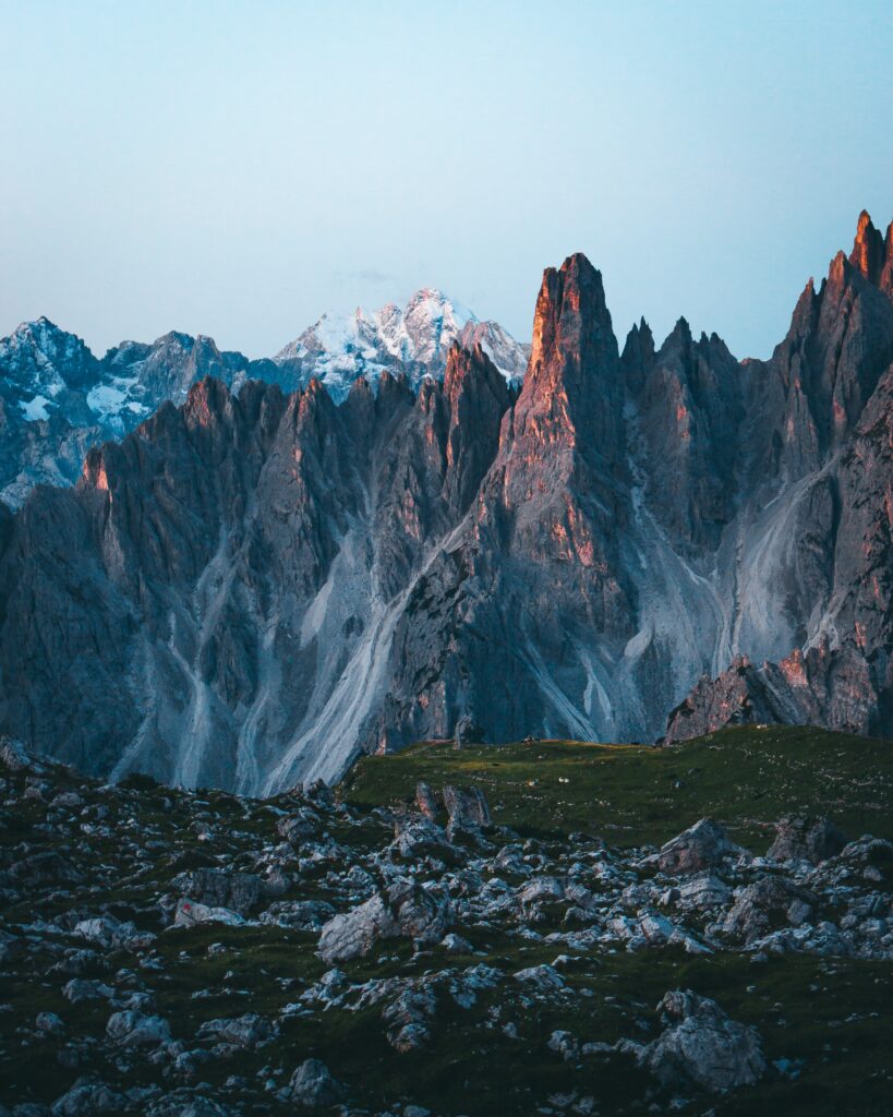Majestic mountain peaks with rugged slopes bathed in warm evening light and green patches Wallpaper