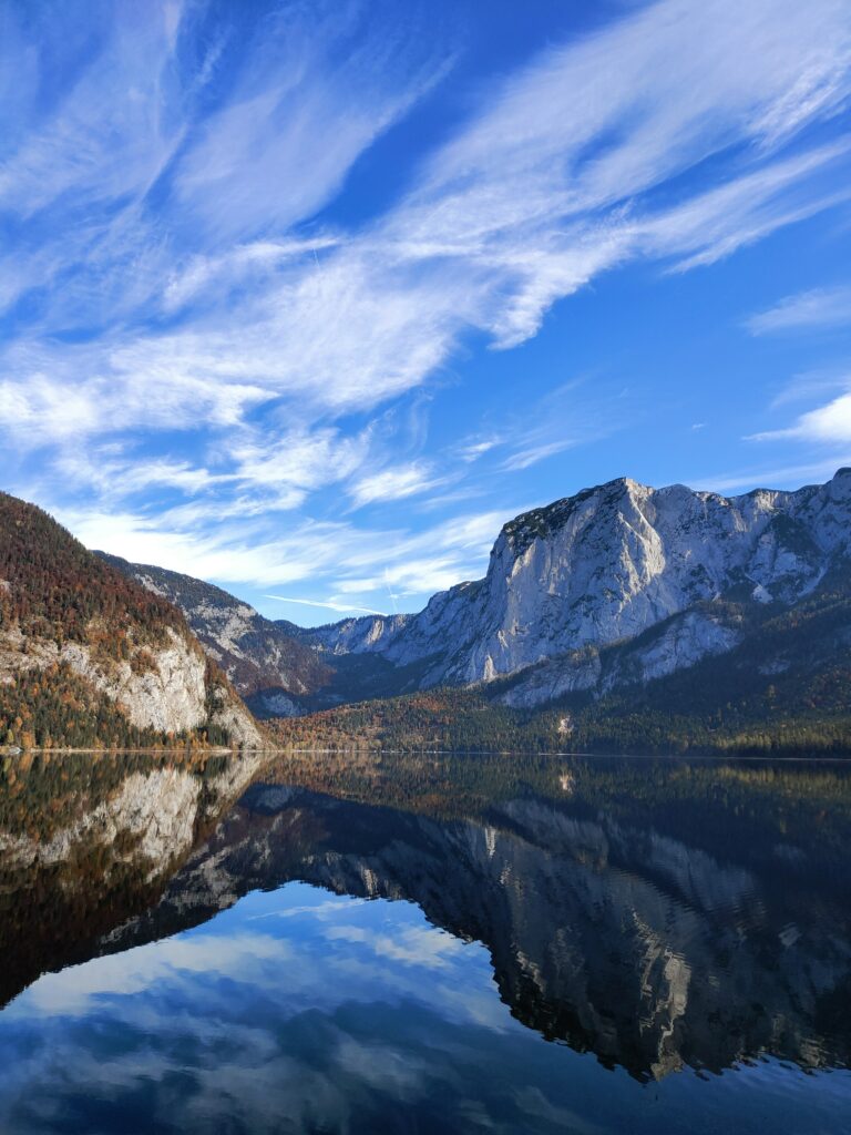 Majestic mountains reflect on a tranquil lake with clear water and wispy clouds serene wallpaper