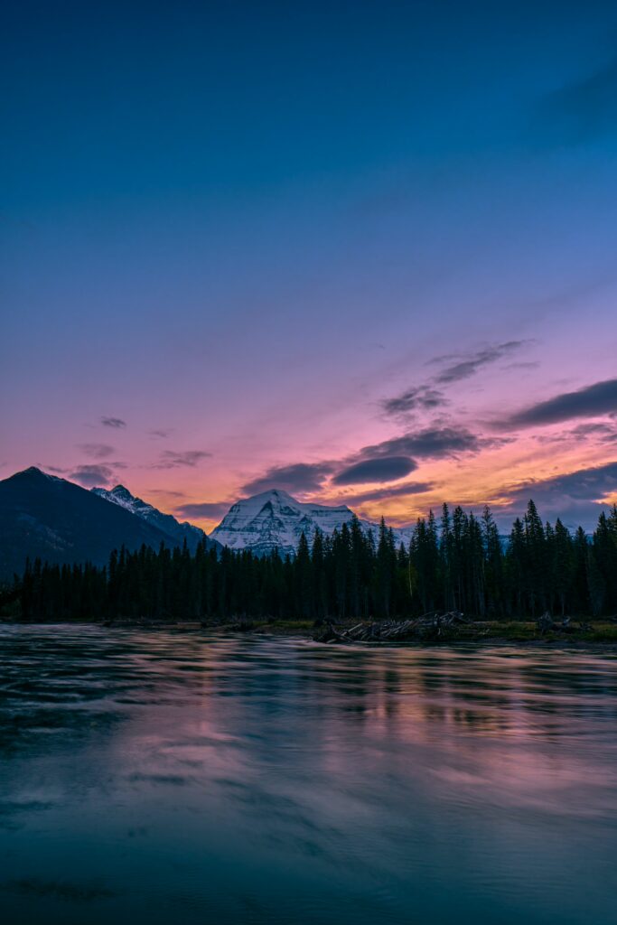 Sunset over serene lake reflecting majestic mountains rugged rocks and dense forest landscape Wallpaper