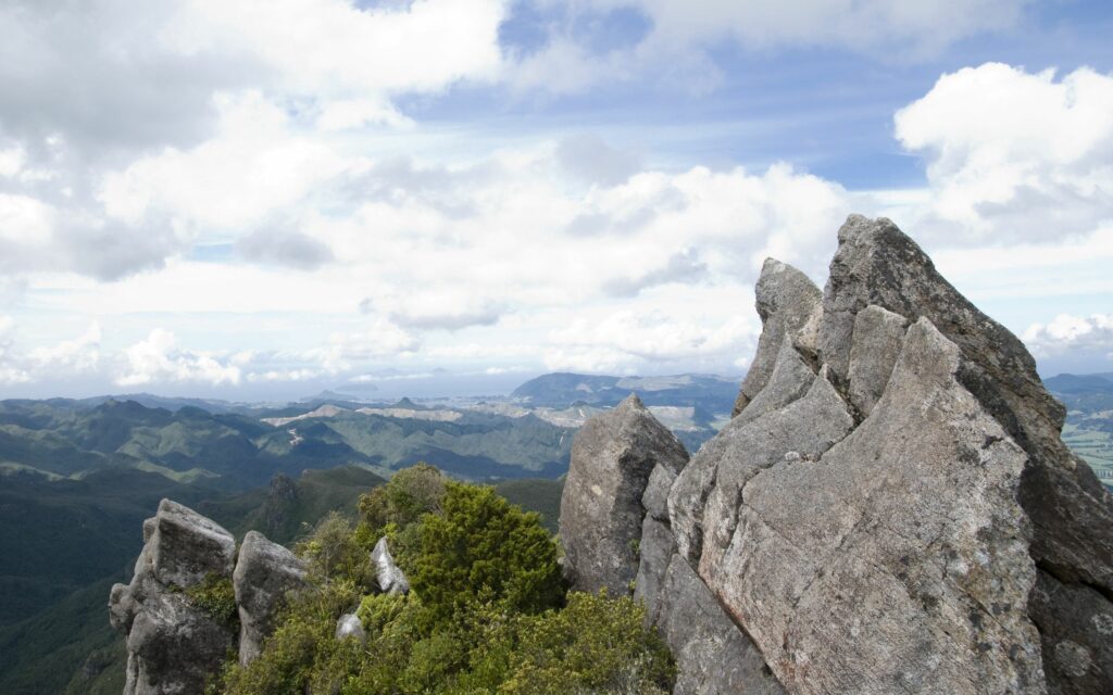 Rugged mountain ridge with rock formations overlooking green valleys and blue sky clouds wallpaper