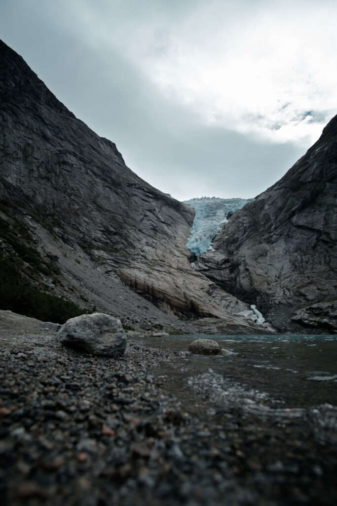 Dramatic rocky shore with glacial water flowing between steep mountains under moody sky wallpaper