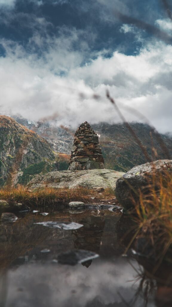 Pile of balanced stones with wild grasses and majestic mountains under a cloudy sky wallpaper