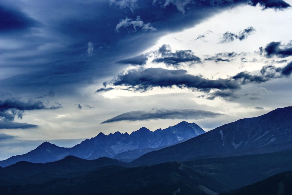Majestic mountain summits under dramatic cloudy skies with deep blue and grey tones wallpaper