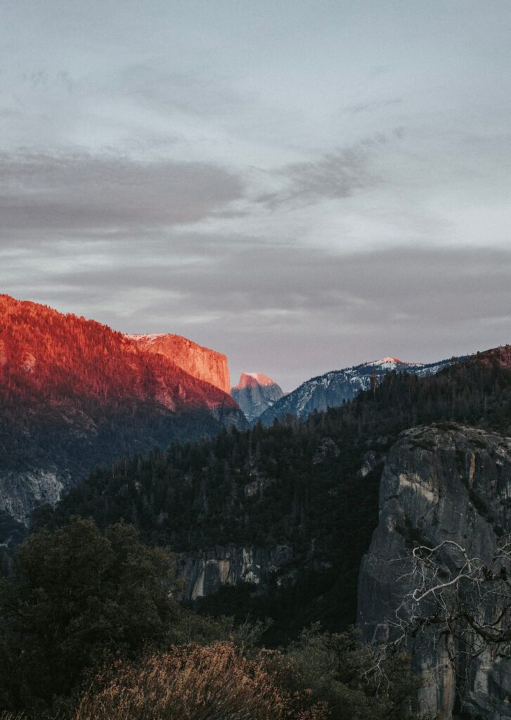 Sunset over towering mountains rugged rocks and dense forest valley scenic nature wallpaper background