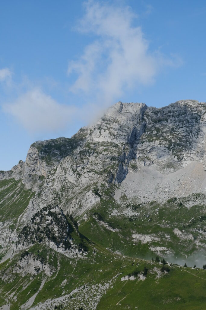 Majestic mountain with rugged gray rocks and green foothills under blue sky with clouds wallpaper