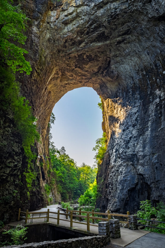 Majestic natural rock arch bridge over forest path with sunlight and lush green trees wallpaper