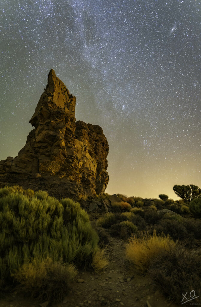 Towering rock formation rises over rugged landscape under starry night sky with earth tones wallpaper