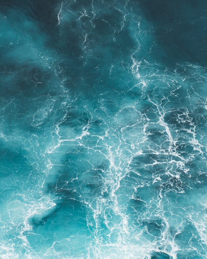 Aerial view of ocean waves with white foam swirling over deep blue and turquoise water wallpaper