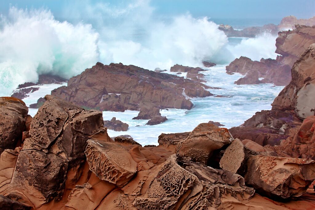 Majestic ocean waves crash on rugged rocks creating splashes in wild coastal seascape wallpaper