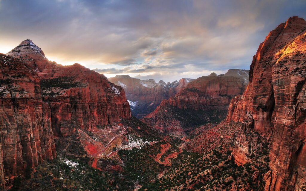 Majestic reddish brown mountains and rugged rocks under dramatic sky with soft sunlight and greenery Wallpaper