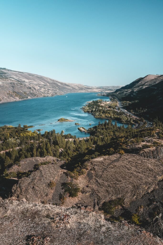 Aerial view of a winding river between rugged hills with lush greenery under clear blue sky wallpaper