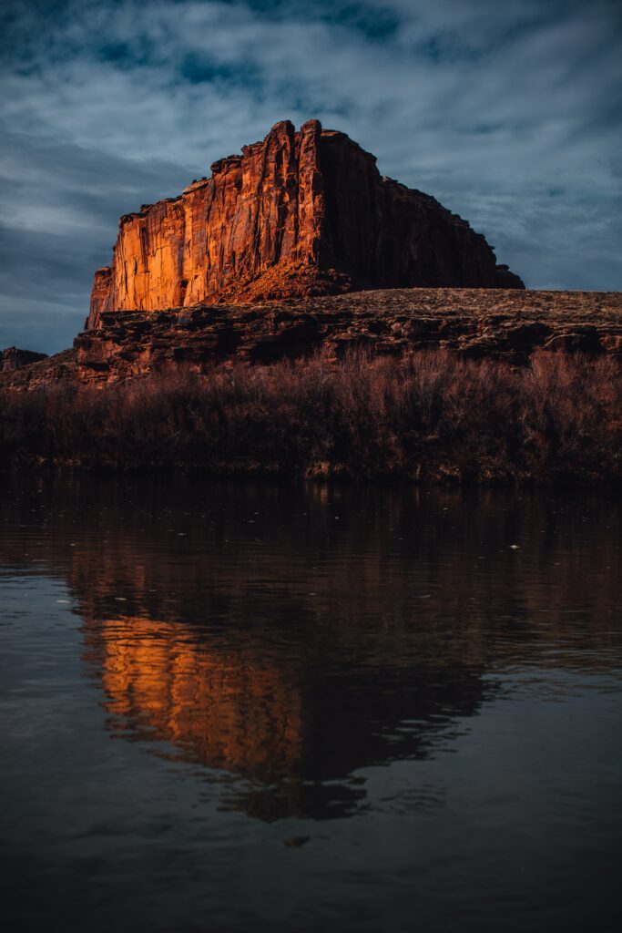 Majestic glowing rock formation reflecting in calm water under dramatic sky wallpaper background