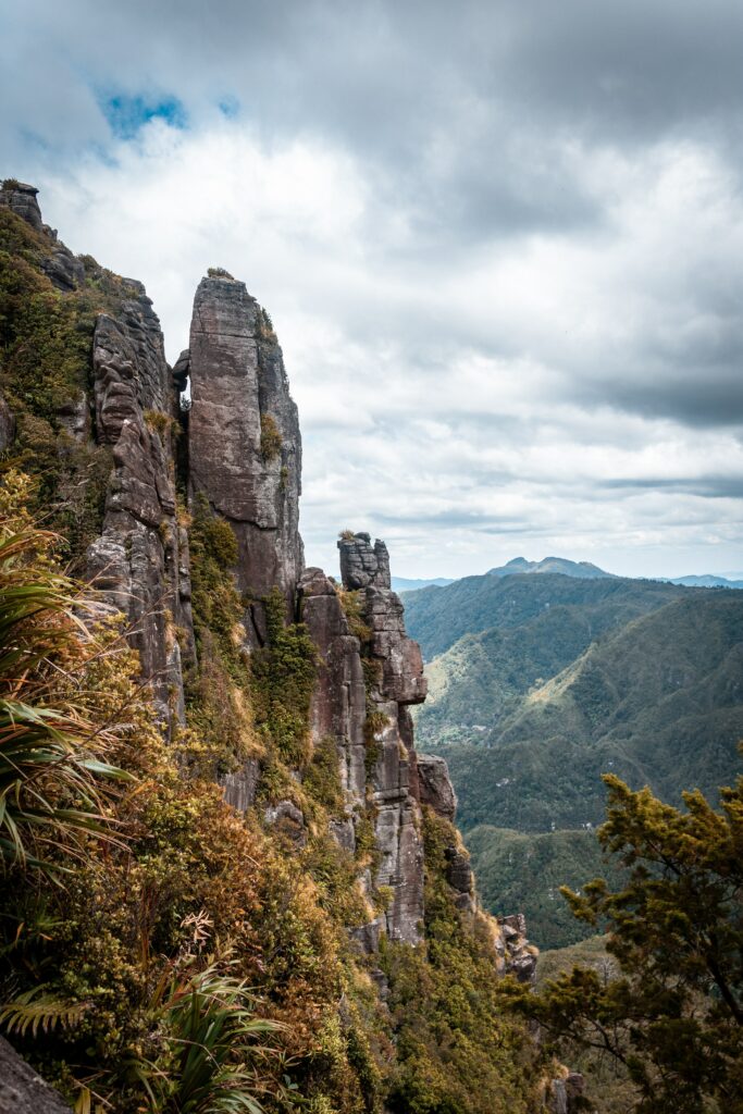 Towering rocky cliffs and rugged green mountains under dynamic clouds showcasing natural beauty Wallpaper