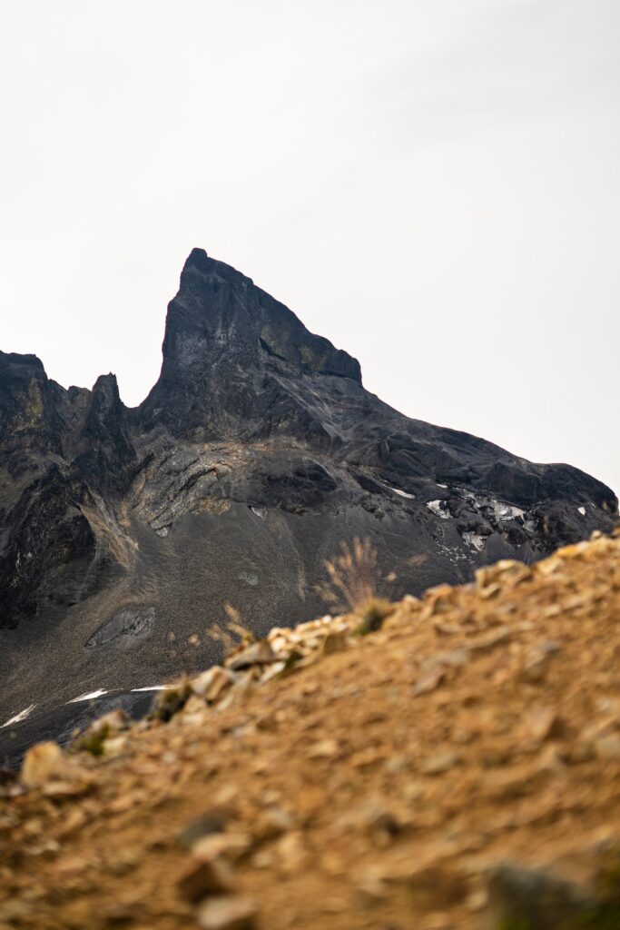 Dramatic rock peak towering over rugged brown and gray mountain slopes steep incline texture Wallpaper