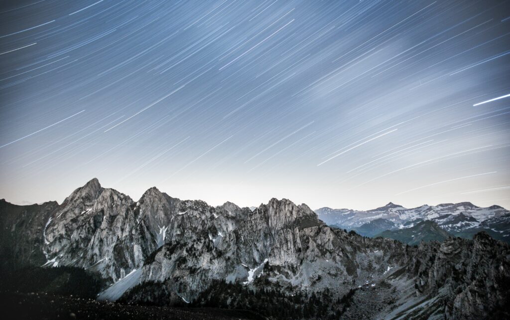 Rugged mountain range with jagged peaks under starry night sky in moody cool tones wallpaper